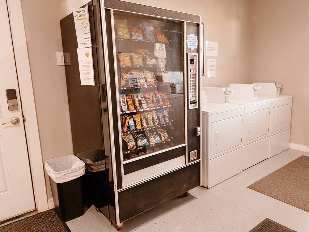 A snack vending machine and dryers in the laundry room