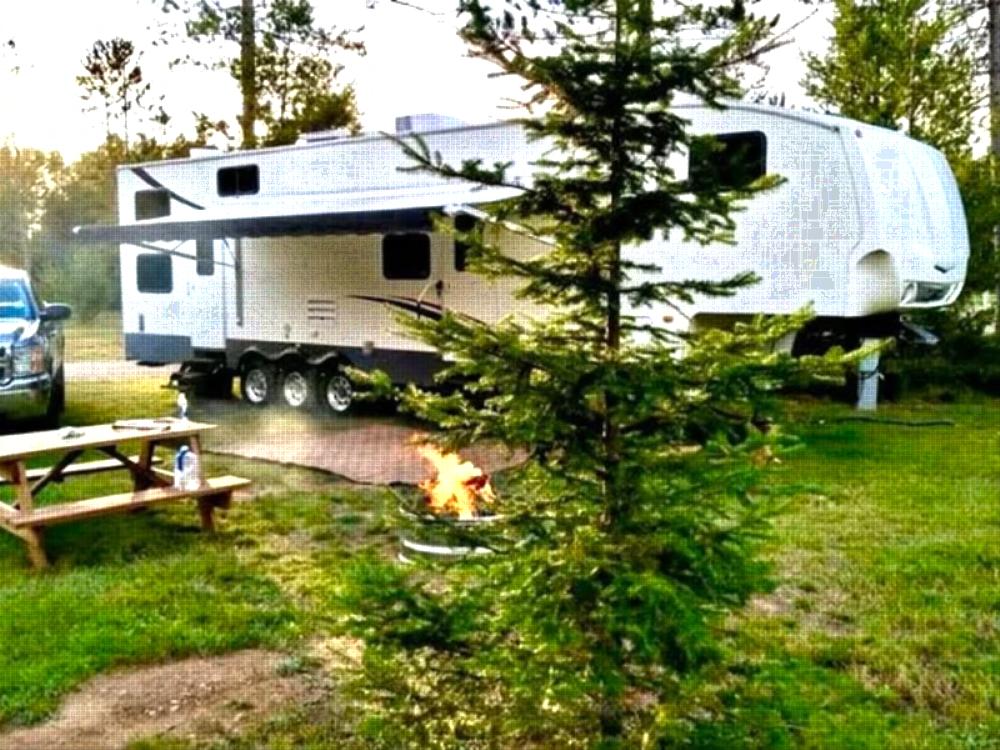 Parked trailer near fire pit and panic table at Plum Pines RV Park & Campground