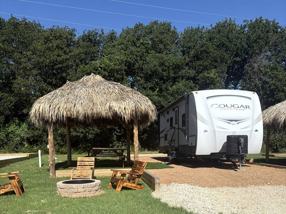 An RV site with Adirondack chairs around a fire ring