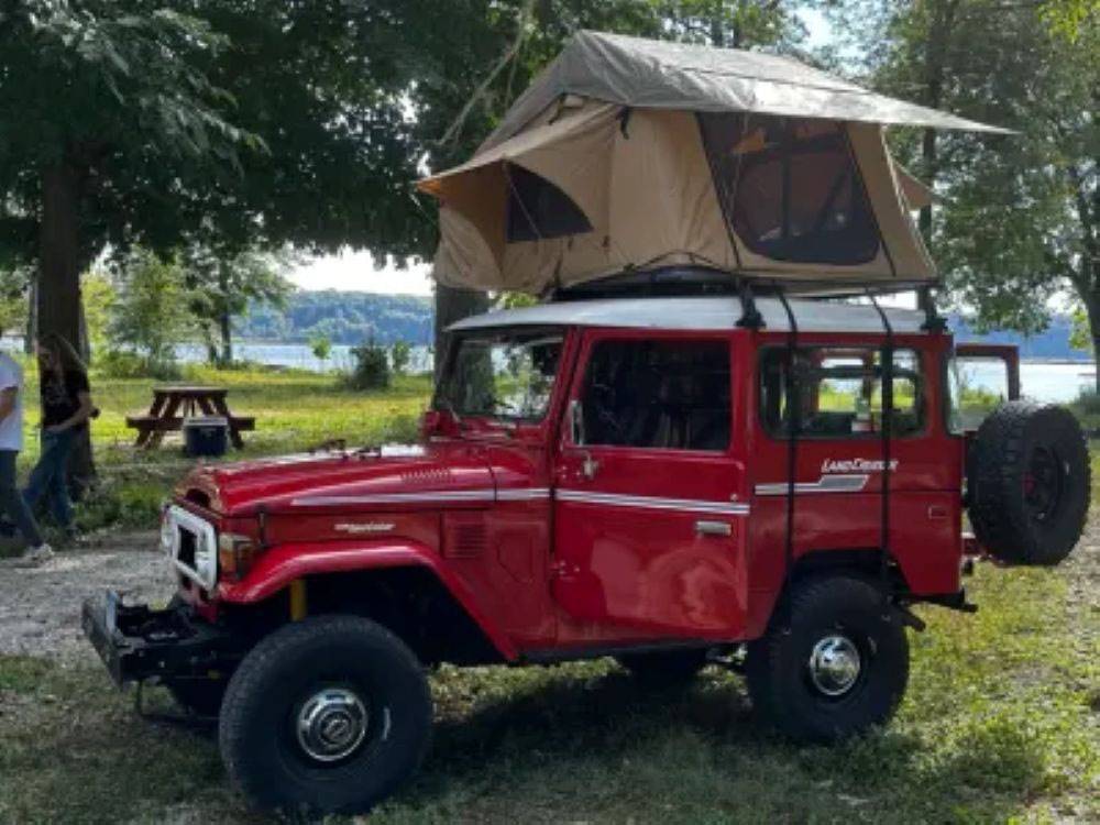 A tent strapped to the top of a red Land Cruiser