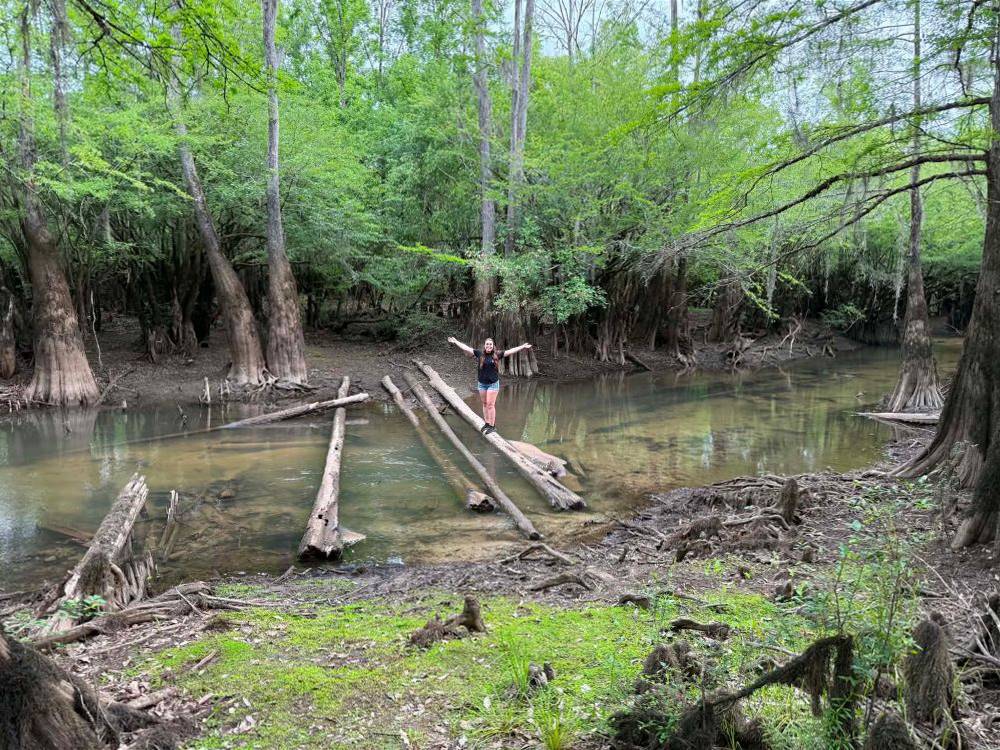 A girl standing on a log crossing the river