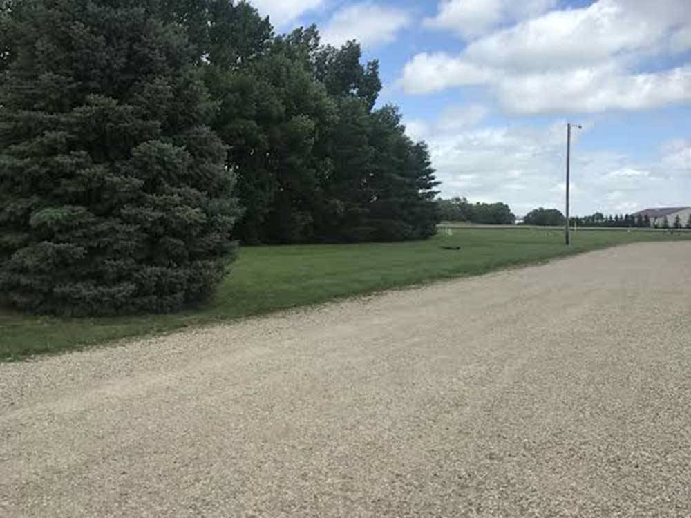 Gravel road next to grassy area with trees at A PRAIRIE BREEZE RV PARK