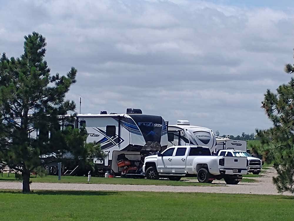 Grassy area with trees and 5th wheels in the distance at A PRAIRIE BREEZE RV PARK