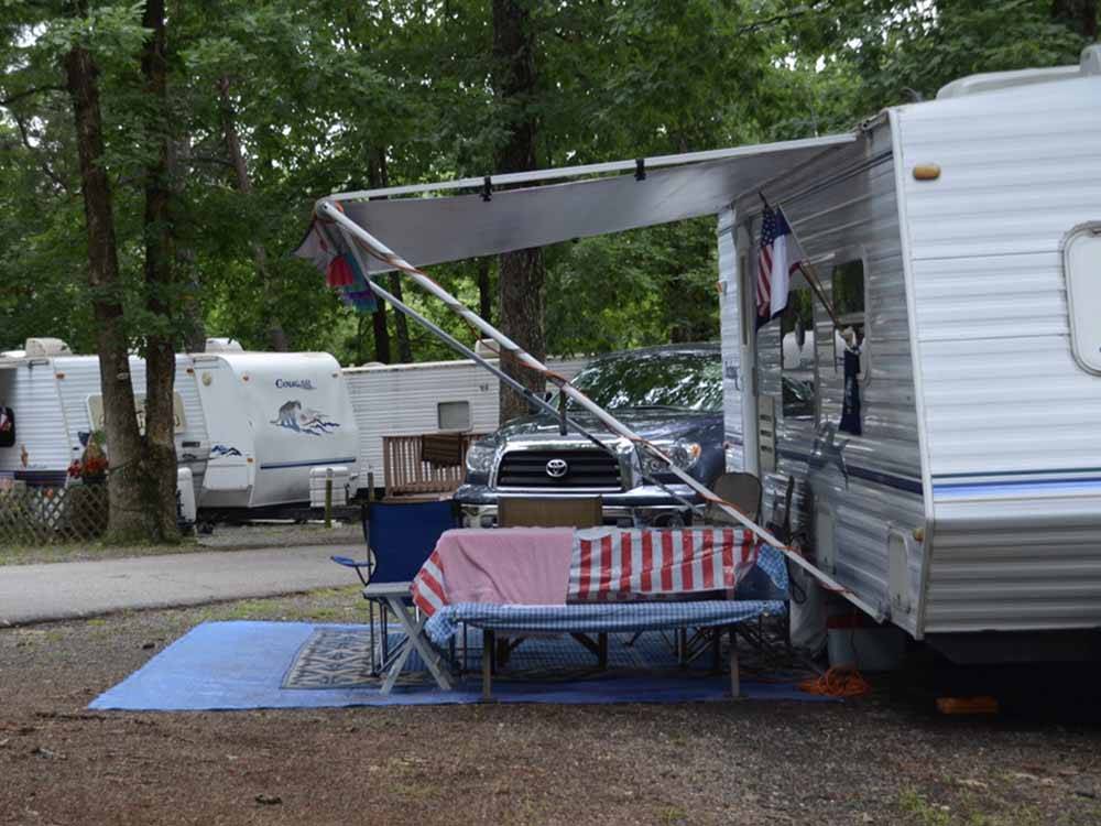 A trailer in a site with a bench and chairs at FORT WILDERNESS CAMPGROUND AND RV PARK