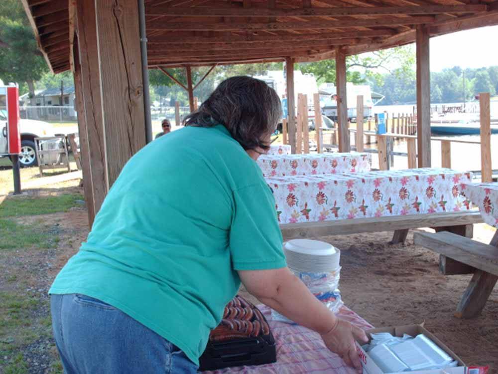 Woman in green shirt setting out hot dogs on tables at MOON LANDING RV PARK & MARINA