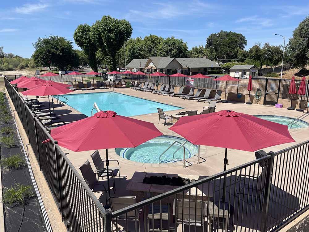 Tables and chairs with red umbrellas around the pool at KINGS RIVER RV RESORT