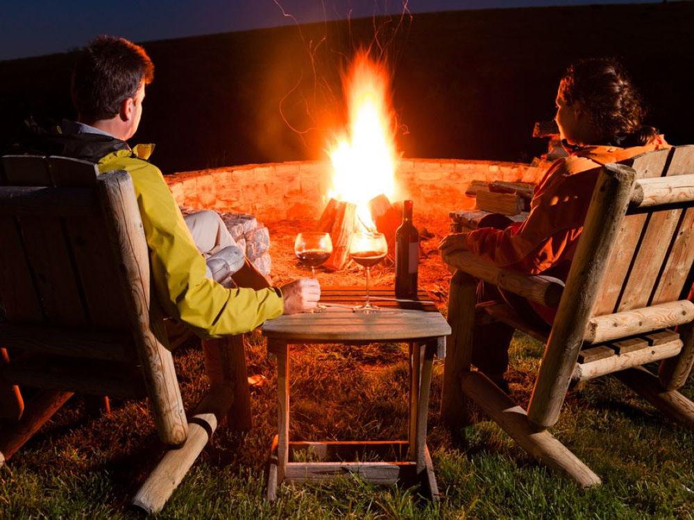 A couple sitting near a fire ring in the evening at ASHLAND/HUNTINGTON WEST KOA HOLIDAY