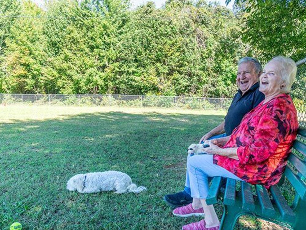 A couple with their dog in the fenced pet area at SWAN CREEK COMMUNITY (MHP)