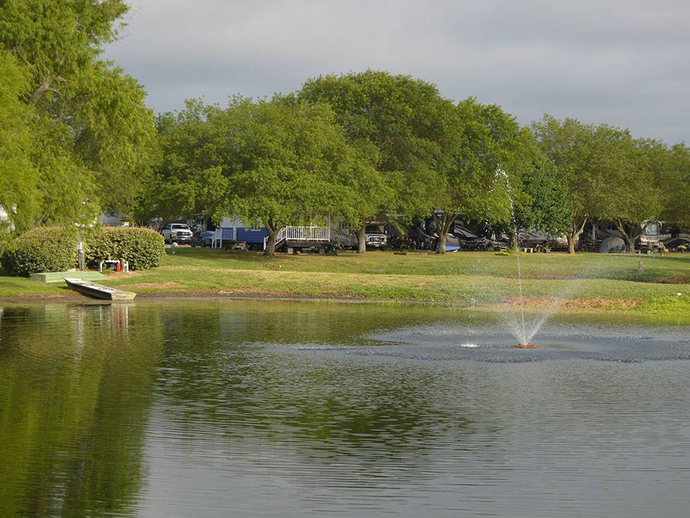 Boat docked at pond with fountain in the middle at BLUEBONNET RIDGE RV PARK & COTTAGES