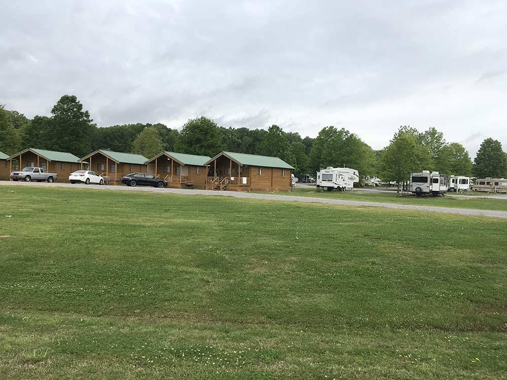 Cars and trailers parked alongside wooden cabins with green roofs at MOVIETOWN RV PARK
