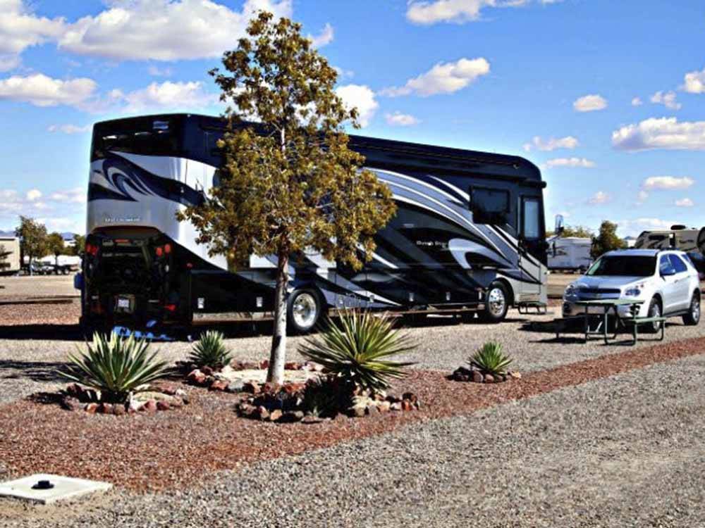 A motorhome and car in a gravel RV site at SONORAN DESERT RV PARK