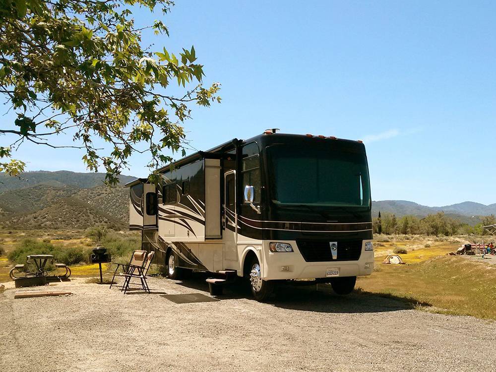 RV parked on lot with picnic table, chairs and grill