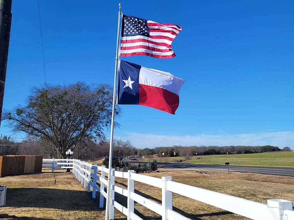 A USA and Texas flag hanging by a white fence at CANTON I-20 RV PARK