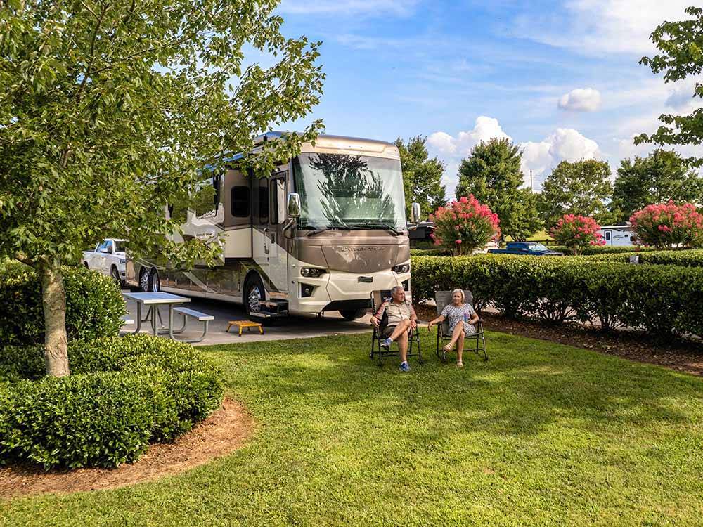 Motorhome in campsite, couple sitting in lawn chairs at TWO RIVERS LANDING RV RESORT