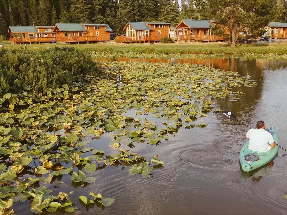 A man kayaking towards a group of rental cabins at SILVER COVE RV RESORT