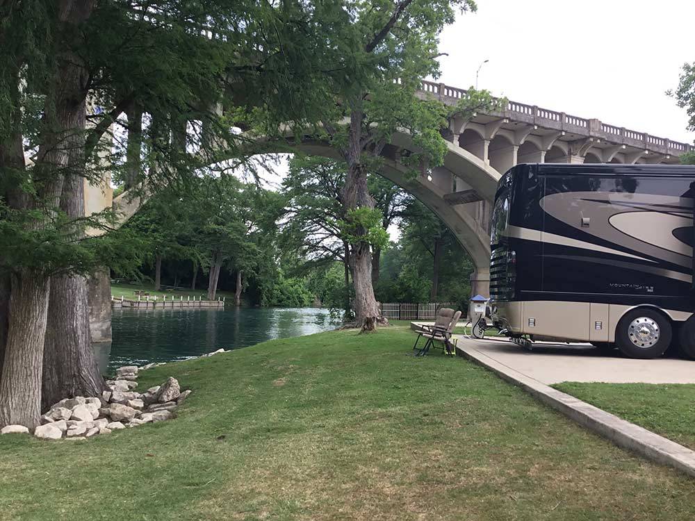 Arching concrete bridge over flowing river with large black RV in foreground at RIVER RANCH RV RESORT
