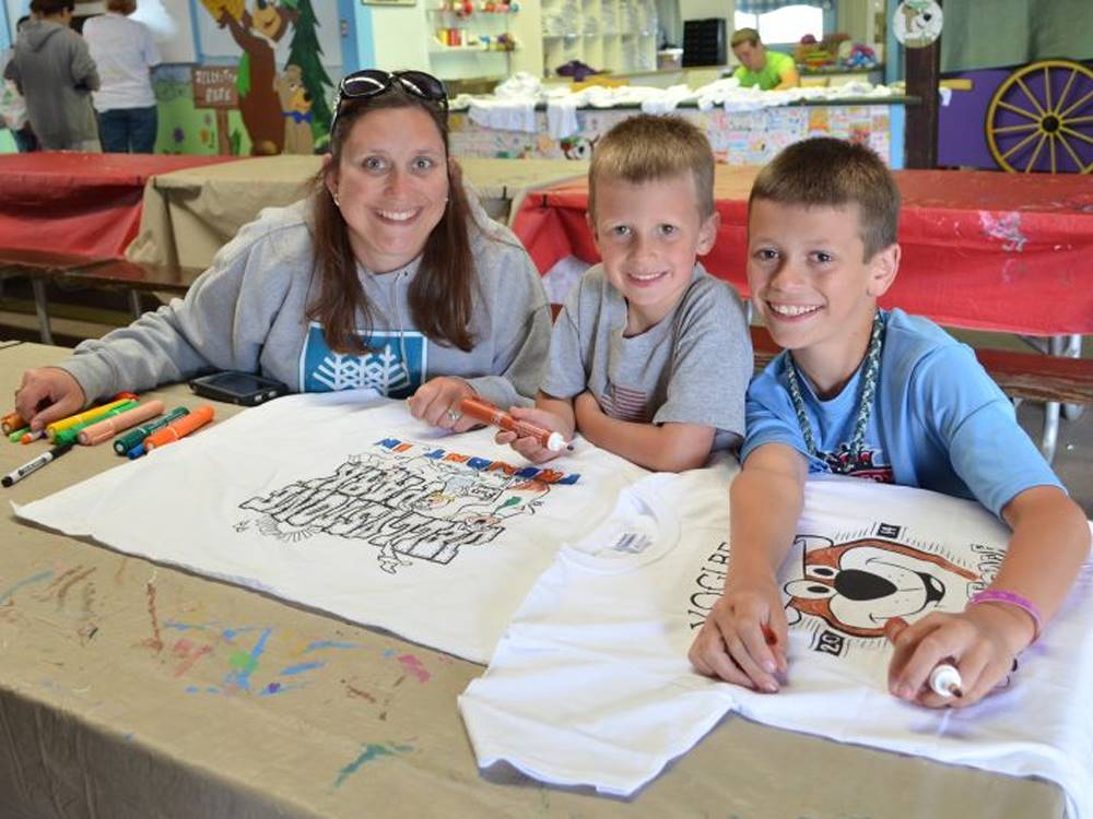 A lady and two boys coloring on a t-shirt at YOGI BEAR'S JELLYSTONE PARK AT DELAWARE BEACH