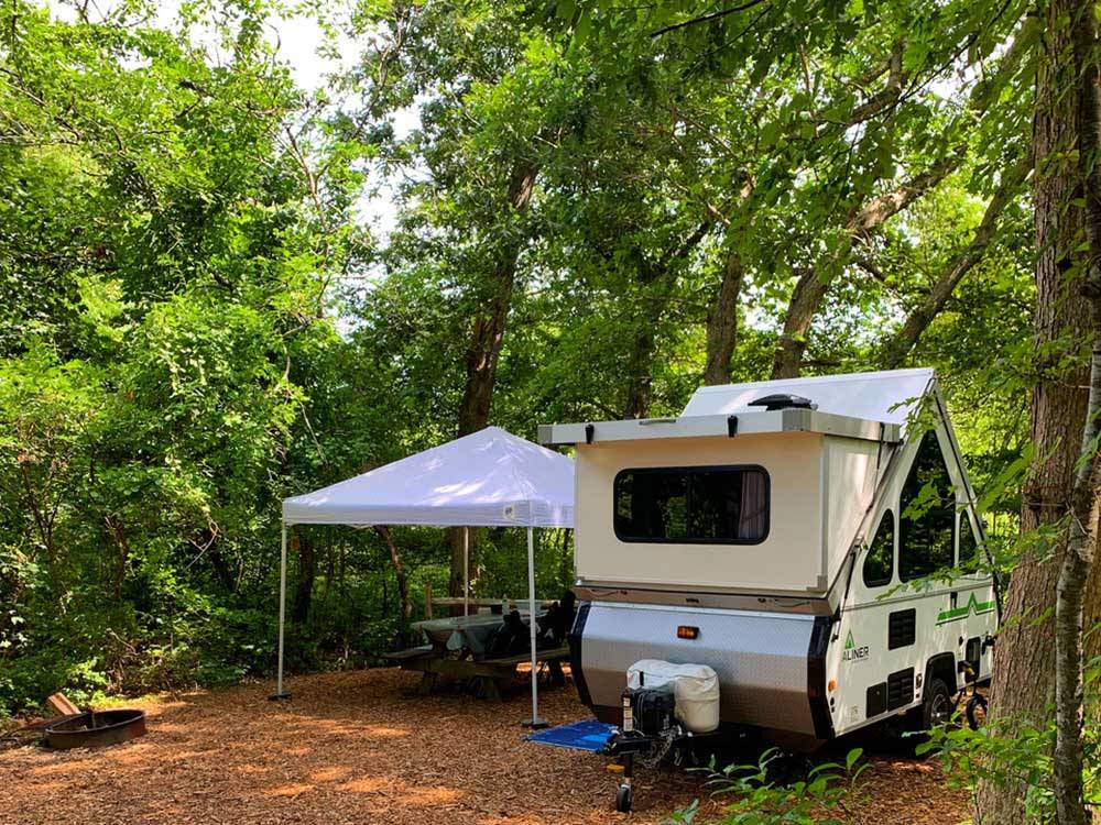 A pop up trailer under trees at SHADY KNOLL CAMPGROUND