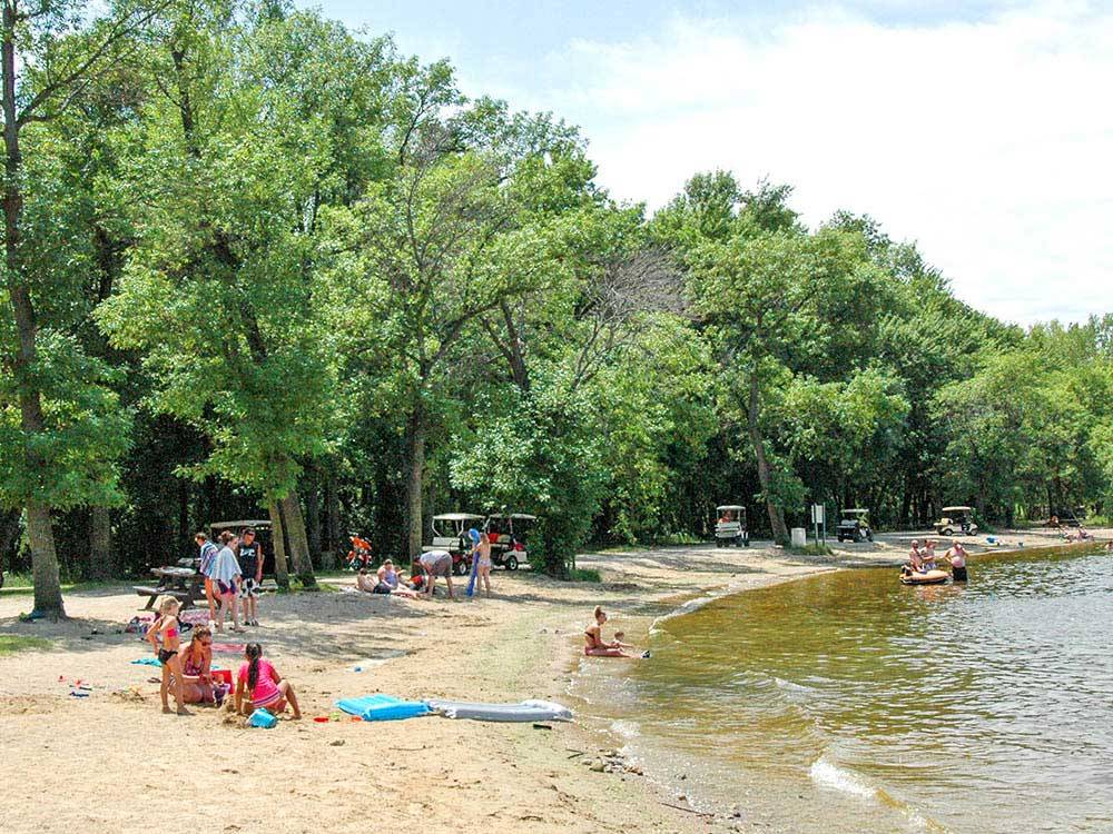 People lakeside surrounded by large trees at LAKELAND CAMPING RESORT