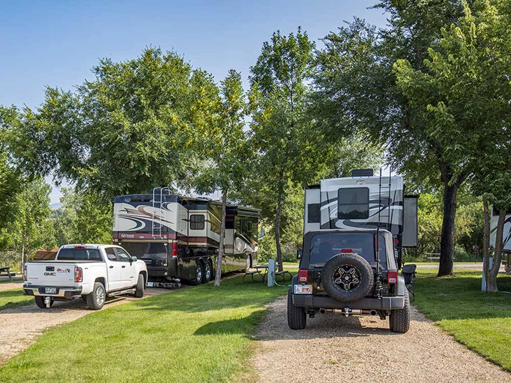 Large RVs in large gravel sites with grass and small trees on either side at CHRIS' CAMP & RV PARK