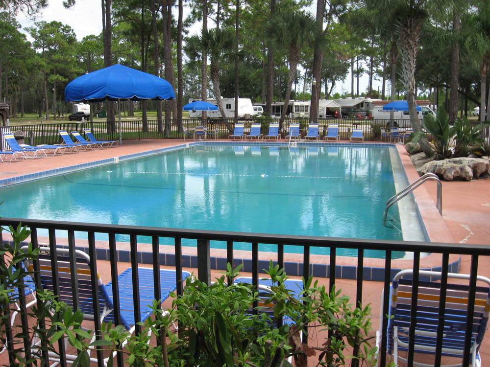 Rectangular swimming pool surrounded by iron fencing and lounge chairs and large shade umbrella at SUNSHINE HOLIDAY DAYTONA RV RESORT