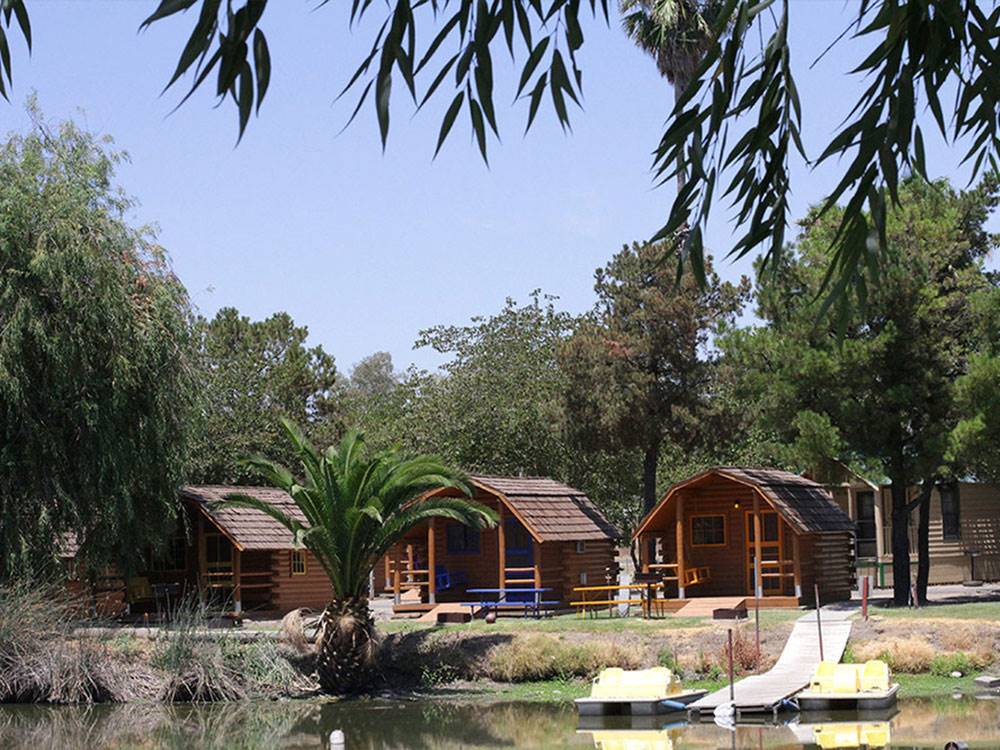 Log cabins along calm water with two pedal boats at end of boat dock at SAC-WEST RV PARK AND CAMPGROUND