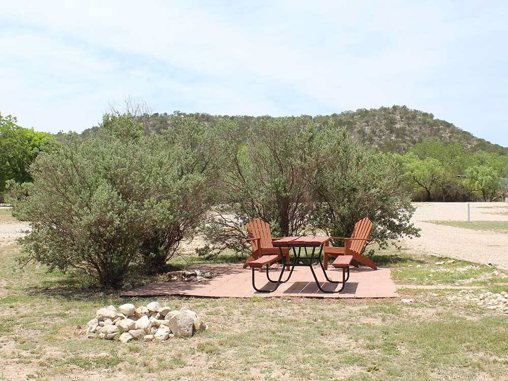 Bench and chairs on a paved patio by a fire pit at NORTH LLANO RIVER RV PARK