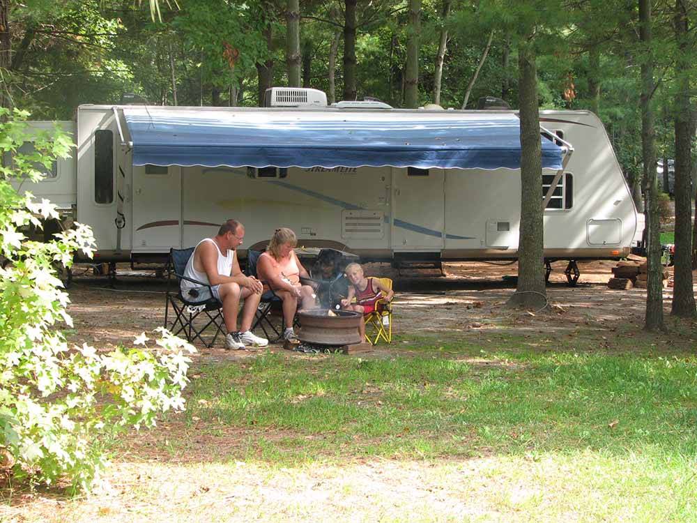 People sitting alongside of a trailer at ACORN CAMPGROUND