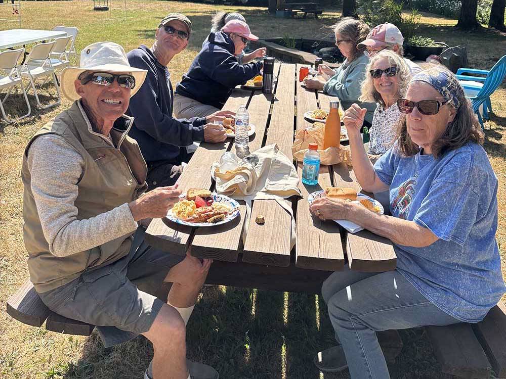 Eight people enjoying a picnic on a sunny day at Port Orford RV Village