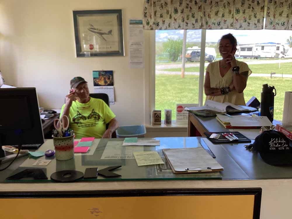 A couple of people behind the registration desk at DEER LODGE A-OK CAMPGROUND