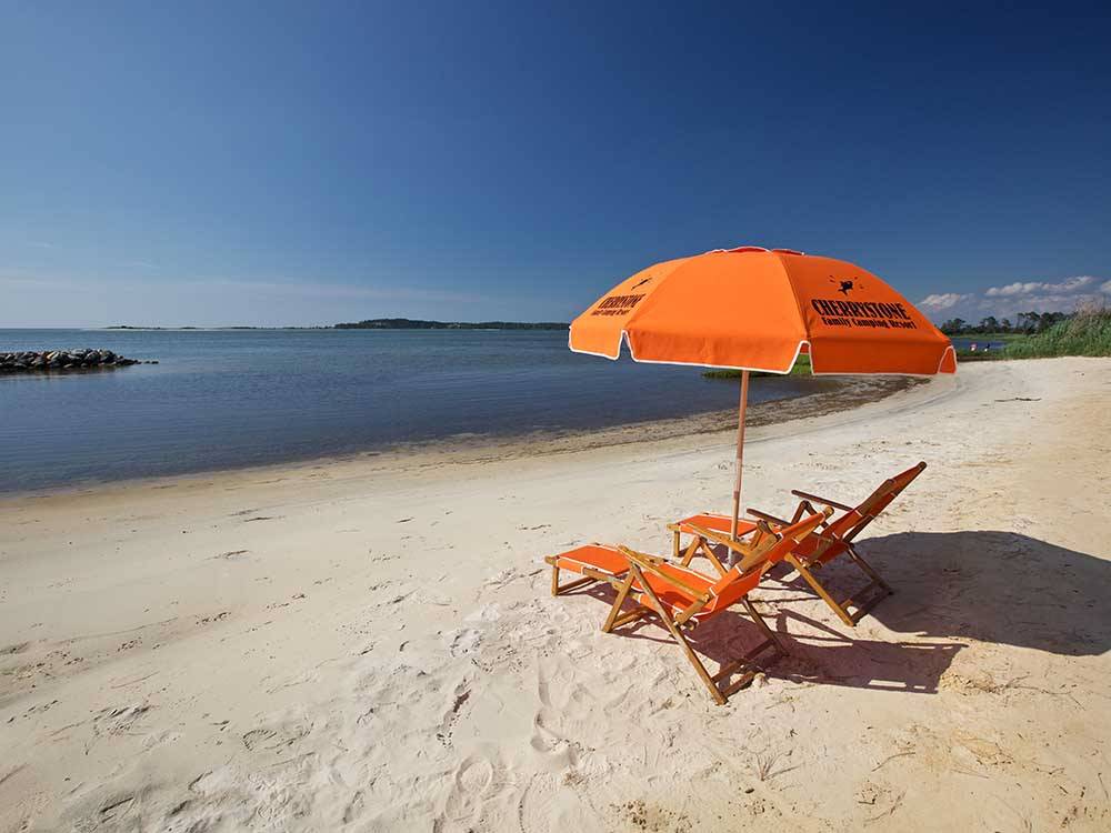 An orange umbrella and two lounge chairs at the beach at SUN OUTDOORS CAPE CHARLES