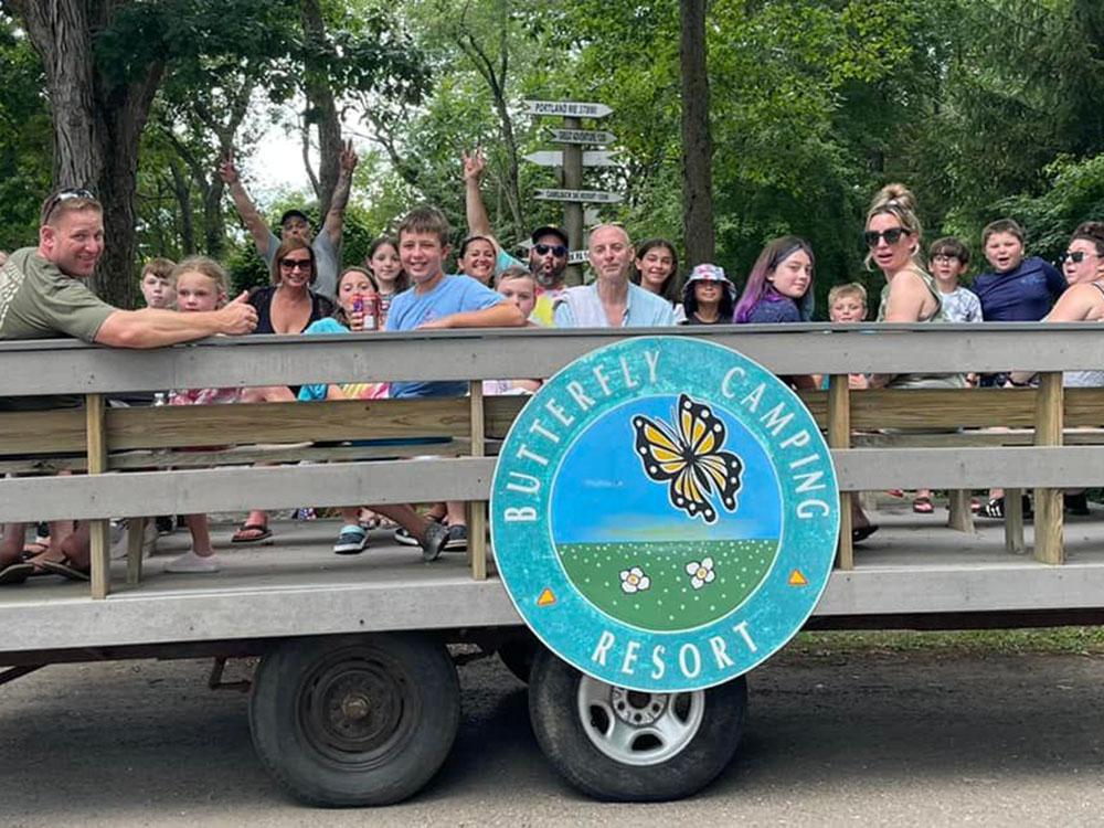 Group of people on wagon ride with campground logo on side of wagon at BUTTERFLY CAMPING RESORT