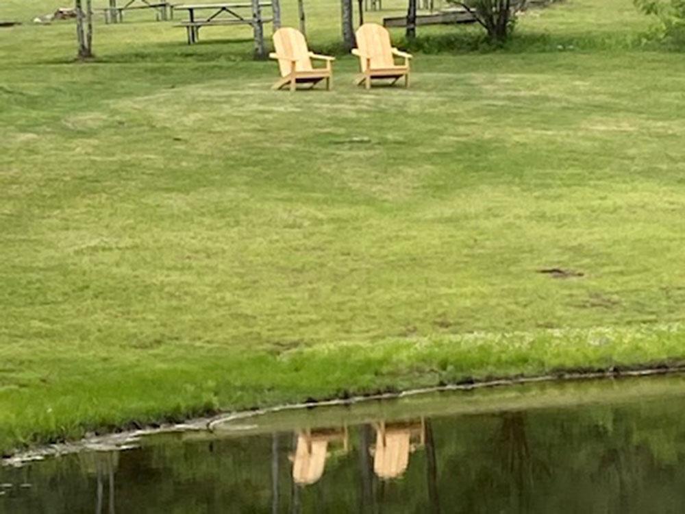 Two wooden Adirondack chairs near the lake at CROW'S NEST CAMPGROUND