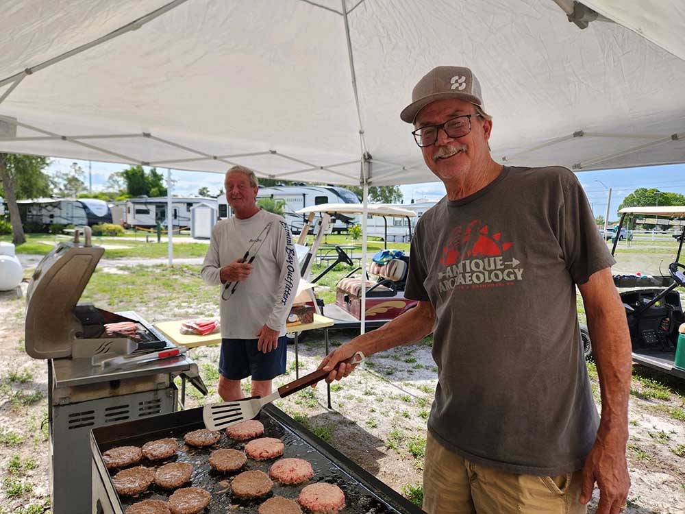 Two men barbecuing hamburgers and hot dogs at CYPRESS CAMPGROUND & RV PARK