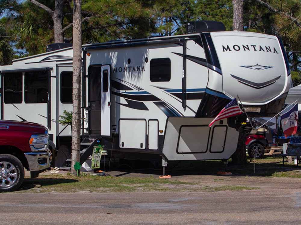 A Montana fifth wheel with flags in a paved site at CAMPER'S INN