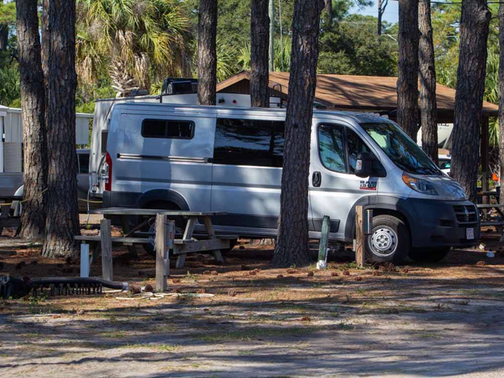 Class B in a gravel site surrounded by tall trees at CAMPER'S INN