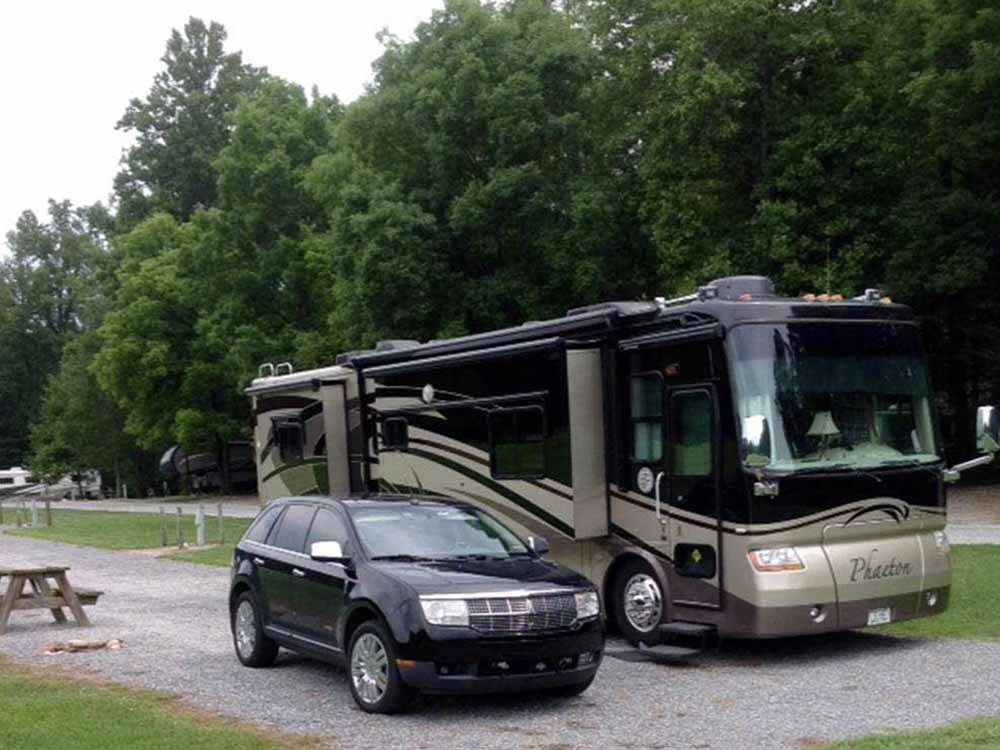 A car parked next to a motorhome in an RV site at BUCK CREEK RV PARK