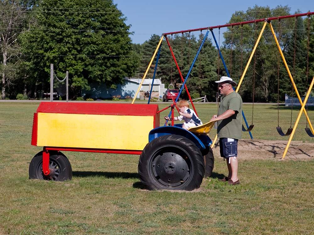A child playing on a tractor while the dad looks on at HOUGHTON LAKE TRAVEL PARK CAMPGROUND