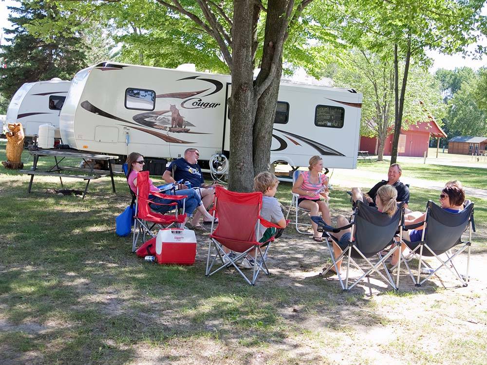 People gathered under a tree by their RV site at HOUGHTON LAKE TRAVEL PARK CAMPGROUND