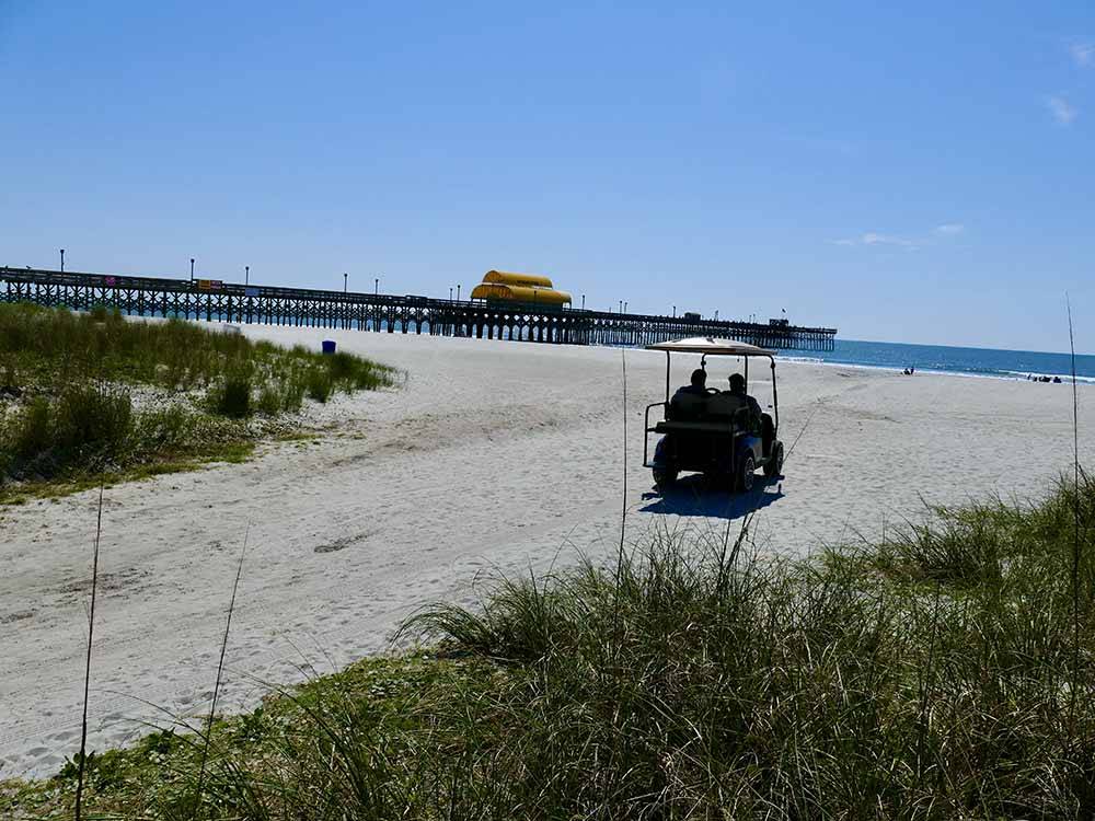 A couple driving a golf cart to the beach at APACHE FAMILY CAMPGROUND & PIER