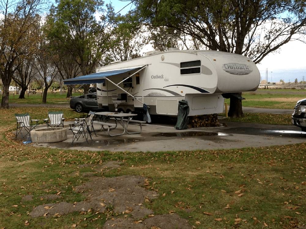 Fifth wheel parked on lot with picnic bench and folding chairs