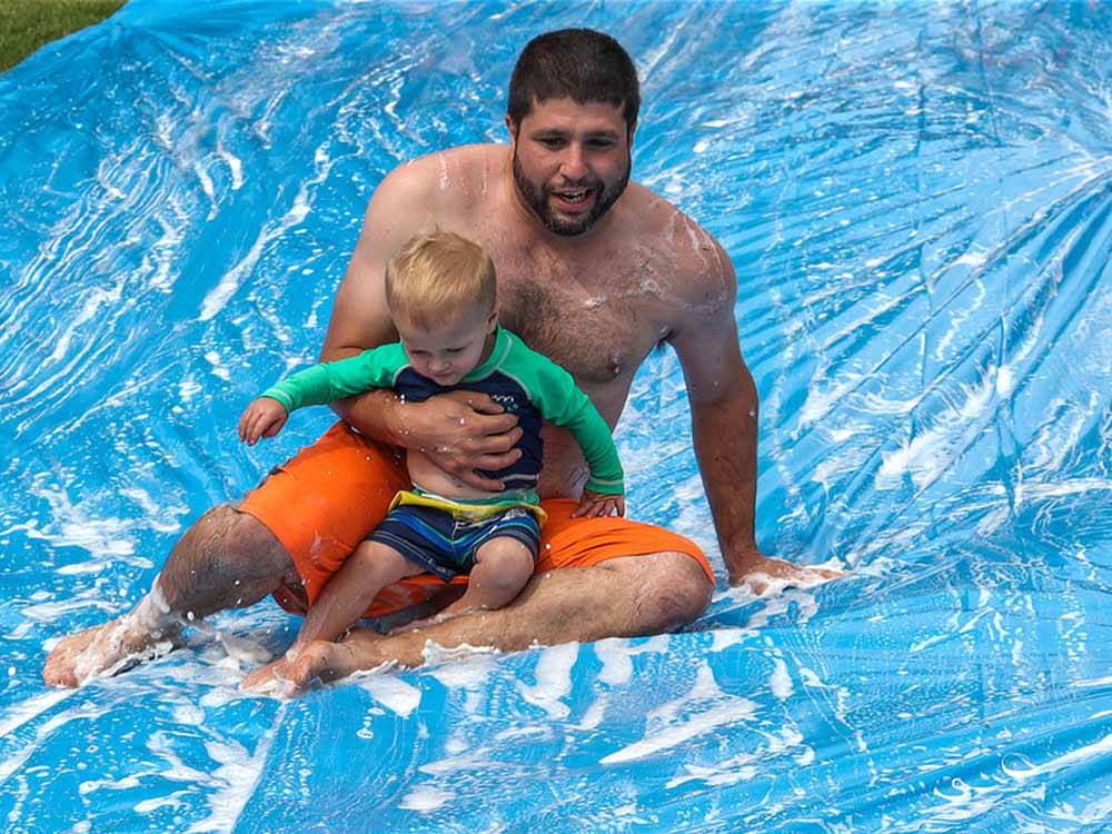 A dad and son going down a slip and slide at COUNTRY ROADS CAMPGROUND
