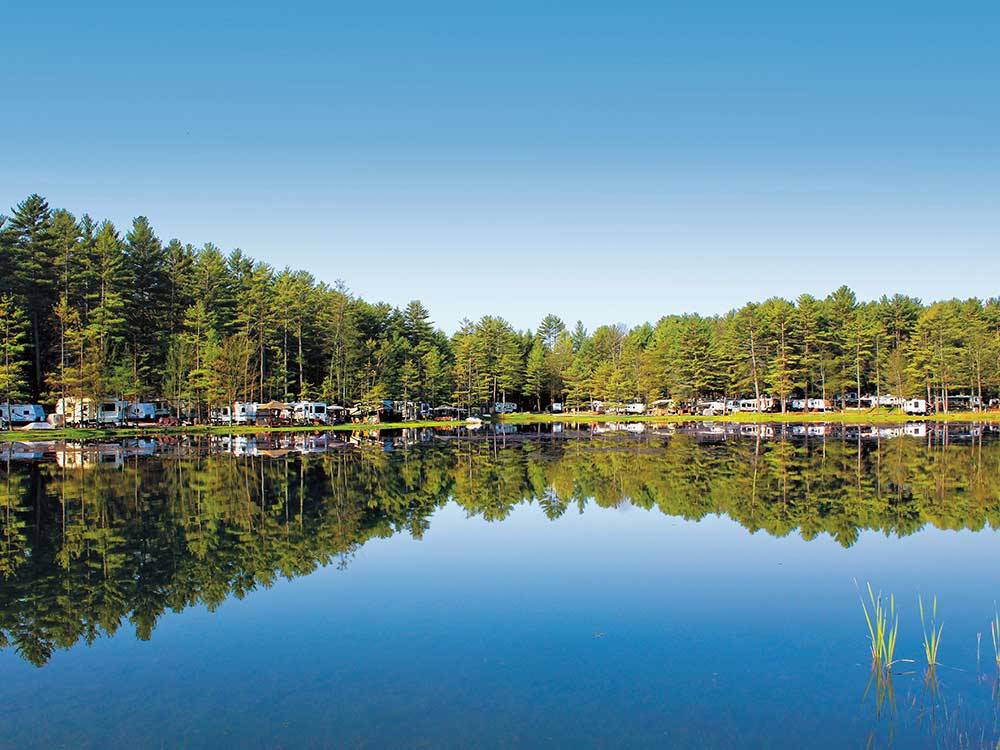 Glassy blue lake with RVs and trailers reflecting on its surface at ALPINE LAKE RV RESORT