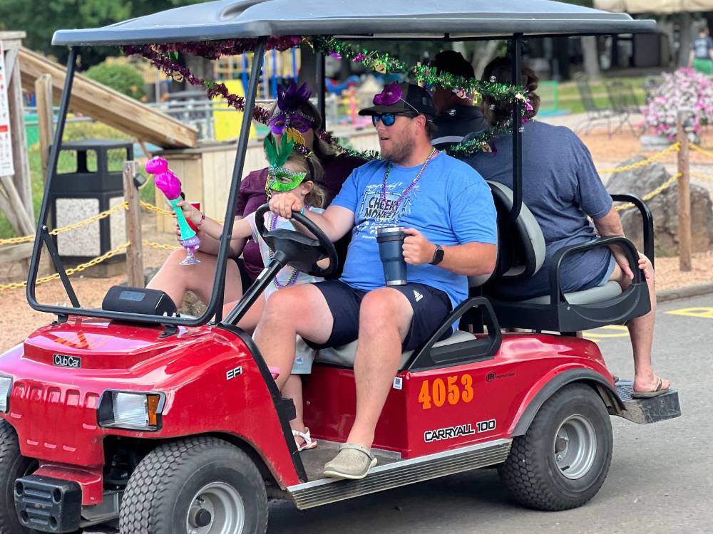 A man driving Mardi Gras revelers in a red golf cart