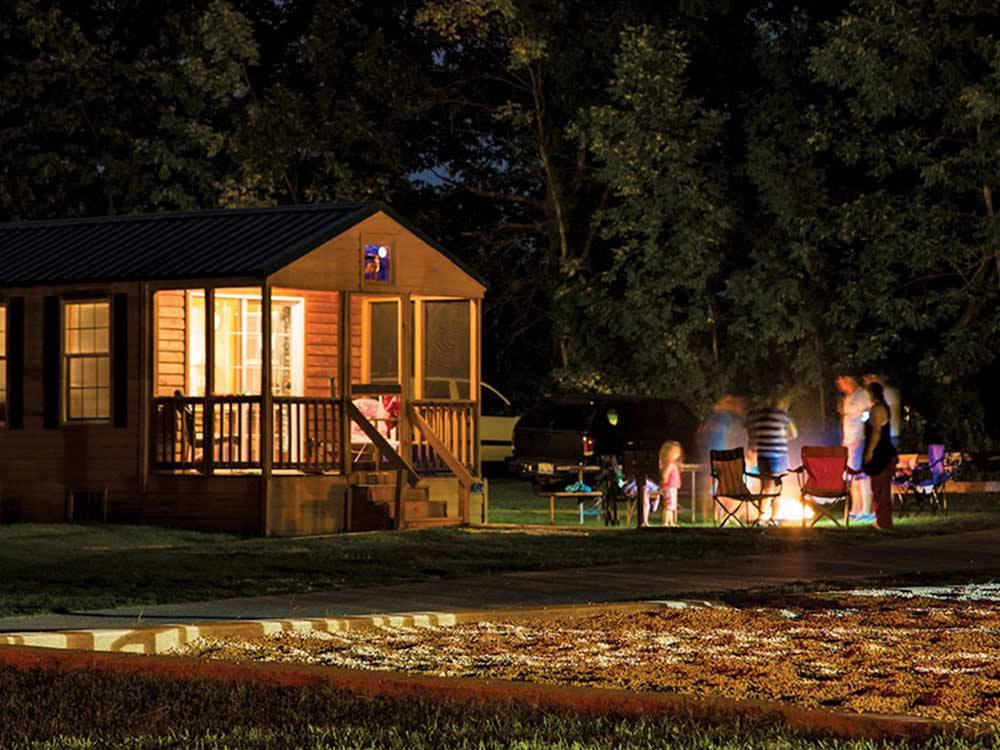 Log cabin with deck with a family standing around a fire pit at PLYMOUTH ROCK CAMPING RESORT