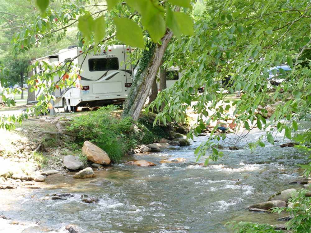 A trailer backed in by a running river at HAPPY HOLIDAY CAMPGROUND
