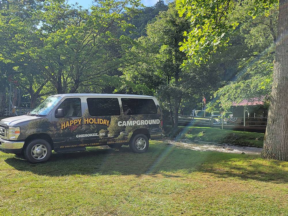 Campground van parked by a tree at Happy Holiday Campground