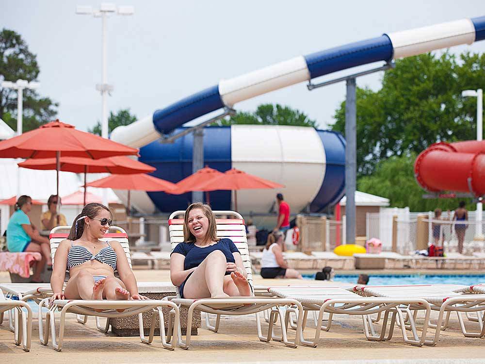 Ladies sunbathing with water slides in the background at BETHPAGE CAMP-RESORT