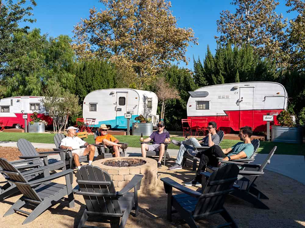 People sitting around a fire pit with vintage trailers in the background at FLYING FLAGS RV RESORT & CAMPGROUND
