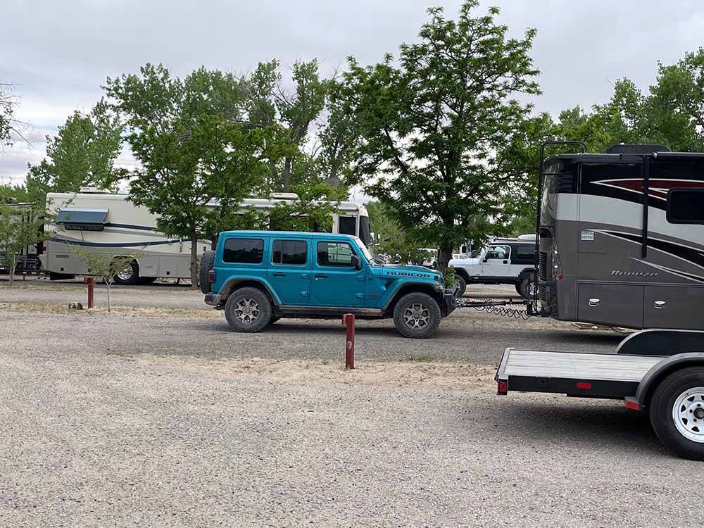 A teal Jeep parked in back of a motorhome in a RV site at SHADY ACRES RV PARK
